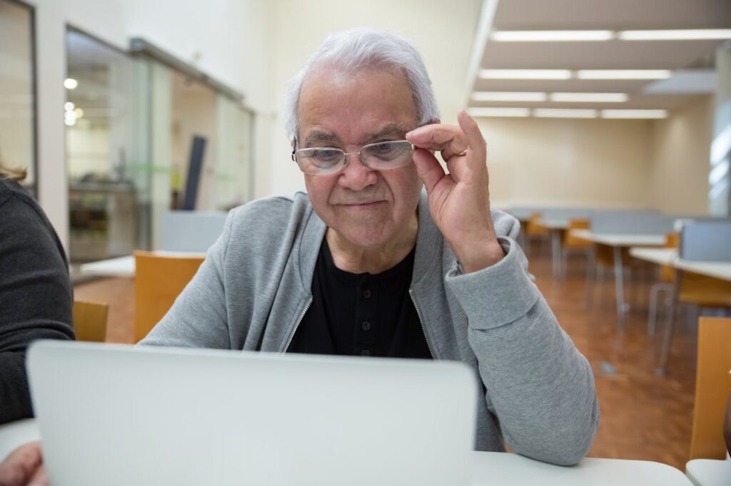 Elderly Man Sitting at the Desk and Using a Laptop